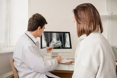 Genç doktor kadın hastaya kalkaneus kırığının röntgen sonucunu açıkla.