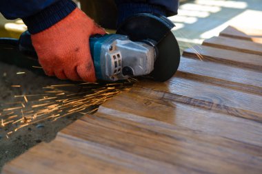 Çalışma sürecini kapatan koruyucu eldivenli işçiler elektrikli açılı öğütücüyle metal bir çatı levhası kesiyorlar. Çatı konsepti