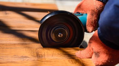 Çalışma sürecini kapatan koruyucu eldivenli işçiler elektrikli açılı öğütücüyle metal bir çatı levhası kesiyorlar. Çatı konsepti