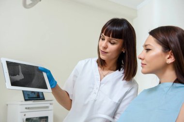 Genç bir dişçi, dişçilik kliniğindeki tablette hastasına dijital diş röntgeni gösteriyor.. 