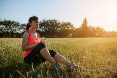 Genç ve güzel bir kadın spor yaptıktan ve gün batımında koştuktan sonra çimlerin üzerinde dinleniyor..