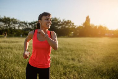 Genç ve güzel bir kadın gün batımında çimlerin üzerinde koşuyor. Her yerde spor yap.