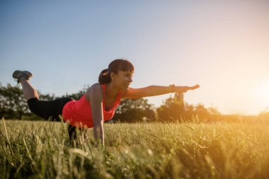 Genç ve güzel bir kadın spor yapıyor. Yoga egzersizlerini parkta çimlerin üzerinde yapıyor. Her yerde spor yap.