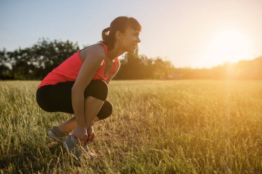 Genç ve güzel bir kadın spor yapıyor, botlarının bağcıklarını doğanın ortasında çimlere bağlıyor ve koşmaya hazırlanıyor. Her yerde spor yap.