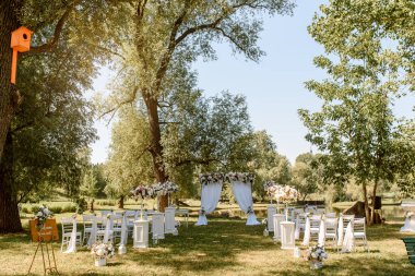 Parkta düğün seremonisi. Güllerle süslenmiş beyaz sandalyeler. Kimse yok.