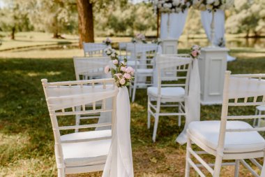 Parkta düğün seremonisi. Güllerle süslenmiş beyaz sandalyeler. Kimse yok.