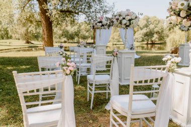 Parkta düğün seremonisi. Güllerle süslenmiş beyaz sandalyeler. Kimse yok.