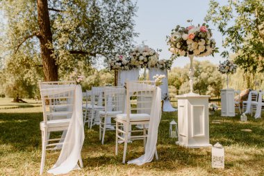 Parkta düğün seremonisi. Güllerle süslenmiş beyaz sandalyeler. Kimse yok.