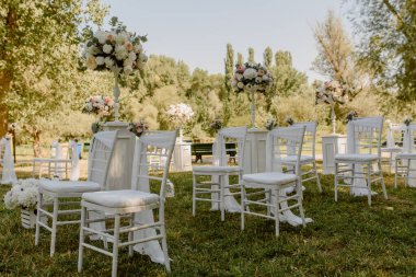 Parkta düğün seremonisi. Güllerle süslenmiş beyaz sandalyeler. Kimse yok.