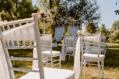 Parkta düğün seremonisi. Güllerle süslenmiş beyaz sandalyeler. Kimse yok.