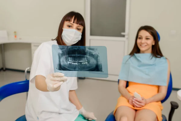 歯科で行う必要があるすべての歯科治療の歯科X線パノラマ画像上の彼女の患者に説明若い女性歯科医 歯科用X線フィルの保持 — ストック写真