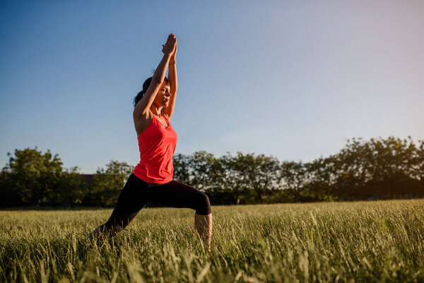 Young beautiful woman is making sport, she is doing the yoga exercises on a grass in the midst of nature on sunset. Make sport every where concept