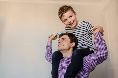 Baba ve oğlunun gülüşlerini yakından çek, çocuk babasının omuzlarında oturuyor.