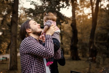Güzel, genç bir anne bebeğini elinde tutuyor ve babası yanında. Mutlu genç aile kavramı. Genç baba ve anne 6 aylık kızlarıyla parkta oynuyorlar.. 