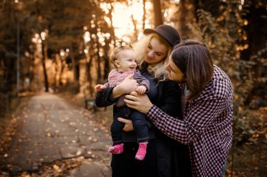 Güzel, genç bir anne bebeğini elinde tutuyor ve babası yanında. Mutlu genç aile kavramı. Genç baba ve anne 6 aylık kızlarıyla parkta oynuyorlar.. 