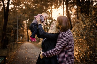 Güzel, genç bir anne bebeğini elinde tutuyor ve babası yanında. Mutlu genç aile kavramı. Genç baba ve anne 6 aylık kızlarıyla parkta oynuyorlar.. 