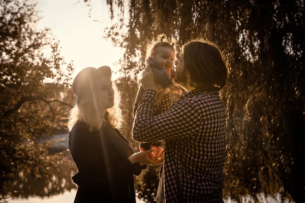Mutlu genç aile kavramı. Genç baba ve anne, 6 aylık kızlarıyla parkta oynuyorlar. Parkta günbatımı.