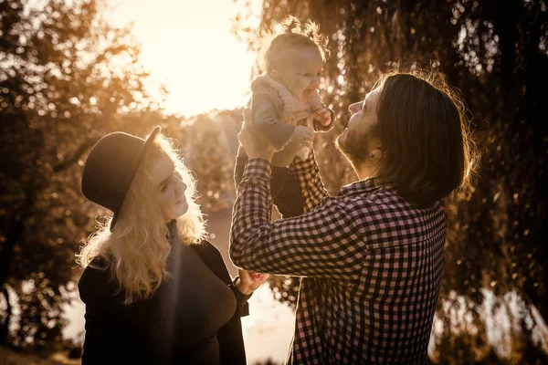 Mutlu genç aile kavramı. Genç baba ve anne, 6 aylık kızlarıyla parkta oynuyorlar. Parkta günbatımı.