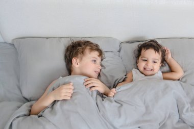 Sabah aile kavramı. Erkek kardeş, beyaz tişörtlü kız kardeş uyanır ve yatakta kameraya gülümser.