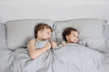 Sabah aile kavramı. Erkek kardeş, beyaz tişörtlü kız kardeş uyanır ve yatakta kameraya gülümser.