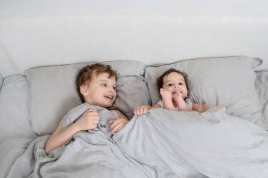 Sabah aile kavramı. Erkek kardeş, beyaz tişörtlü kız kardeş uyanır ve yatakta kameraya gülümser.