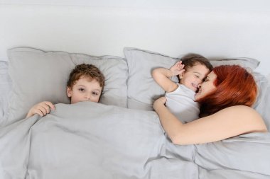Sabah aile kavramı. Anne ve kızının beyaz t-shirtlerle uyanması, gülümsemesi, öpüşmesi ve eğlenmesi.
