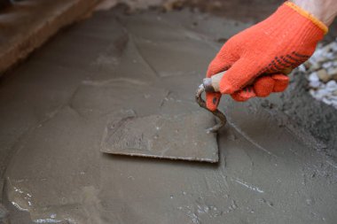 Koruyucu eldivenli bir müteahhit elinde malayla çimentoyu düzleştiriyor.