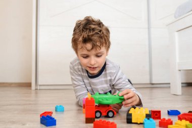 Küçük mutlu çocuk tahta zeminde yatıyor ve oyuncak uçak ve plastik tuğlalarla oynuyor.
