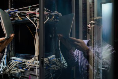 Sunucu odasındaki değişikliklerle ilgili fotoğraf. Bir teknisyen / Gözlüklü bir mühendis defteri tutun ve sunucu hatasını bağlayan veya düzelten interneti ayarlayın.