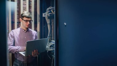 Sunucu odasındaki değişikliklerle ilgili fotoğraf. Bir teknisyen / Gözlüklü bir mühendis defteri tutun ve sunucu hatasını bağlayan veya düzelten interneti ayarlayın.