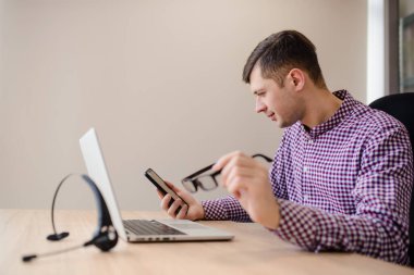 Sıradan gömlekli, gözlüklü ve ofisteki akıllı telefona bakan yakışıklının yüzünü kapat. Seçici odak