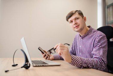 Kapalı tişörtlü, gözlüklü ve ofisteki akıllı telefona bakan yakışıklı bir adam.. 