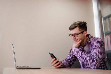 Yaklaş genç yakışıklı, rahat gömlekli, akıllı telefon tutan ve ofiste gülümseyen adam..