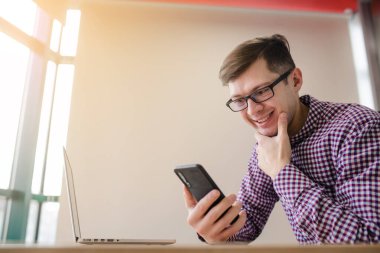 Yaklaş genç yakışıklı, rahat gömlekli, akıllı telefon tutan ve ofiste gülümseyen adam..