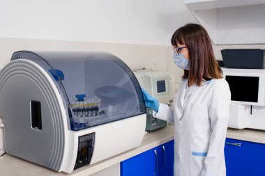 Hastanenin laboratuvar çalışma sürecinde, genç bir kadın laboratuvar asistanı kan testi için bağışıklık testleri ekipmanları için tam otomatik teşhis sistemini çalıştırıyor..