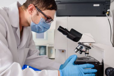 Hastane laboratuarlarında çalışan genç bir doktor kan testinin mikroskobuna bakıyor..