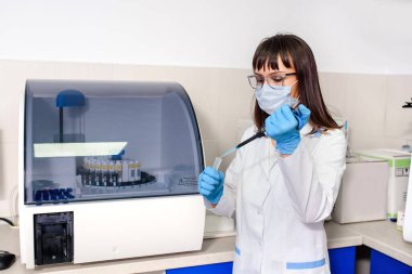 Genç doktor laboratuvar asistanı bağışıklık testleri için tam otomatik bir teşhis sisteminin yanında mikropipet test tüpleri kullanıyor. Hastane laboratuvarları araştırma süreci.