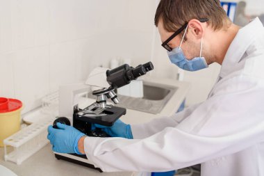Hastane laboratuarlarında çalışan genç bir doktor kan testinin mikroskobuna bakıyor..