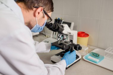 Hastane laboratuarlarında çalışan genç bir doktor kan testinin mikroskobuna bakıyor..