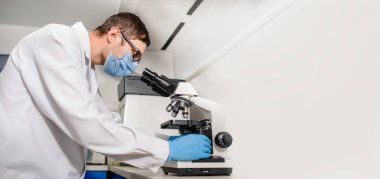 Hastane laboratuarlarında çalışan genç bir doktor kan testinin mikroskobuna bakıyor..