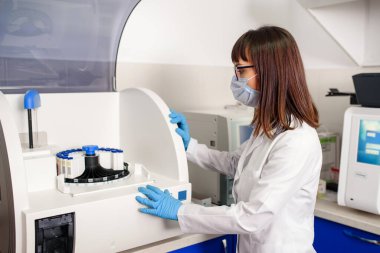 Hastanenin laboratuvar çalışma sürecinde, genç bir kadın laboratuvar asistanı kan testi için bağışıklık testleri ekipmanları için tam otomatik teşhis sistemini çalıştırıyor..