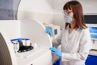 Hastanenin laboratuvar çalışma sürecinde, genç bir kadın laboratuvar asistanı kan testi için bağışıklık testleri ekipmanları için tam otomatik teşhis sistemini çalıştırıyor..