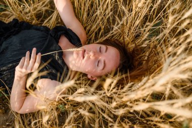 Siyah elbiseli genç bir kadın buğday tarlasında yatıyor..