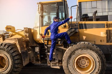 Genç müteahhit inşaat alanındaki buldozer kulübesine tırmanıyor.