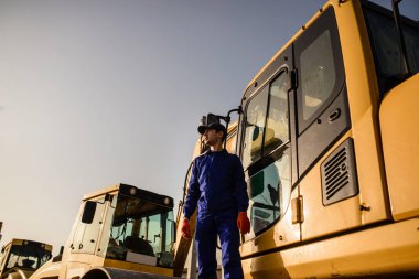 İnşaat alanında çalışma süreci. Bir müteahhit kazıcının yanında oturuyor. İnşaat makineleri konsepti