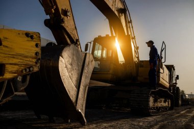 Sunset on the construction site. Silhouette of a contractor builder is sitting near bulldozer. Construction machinery concept clipart