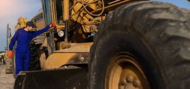 İnşaat alanında mavi tulumlu genç bir müteahhit buldozer tekerleğine bakıyor..