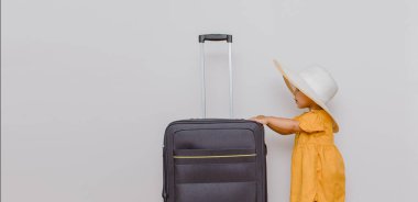 Büyük bir bavulun yanında beyaz şapkalı küçük bir kız. Çocuklar bir tatil konsepti istiyor. Beyaz arkaplan kopyalama alanı