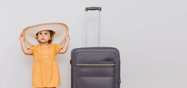 Büyük bir bavulun yanında beyaz şapkalı küçük bir kız. Çocuklar bir tatil konsepti istiyor. Beyaz arkaplan kopyalama alanı