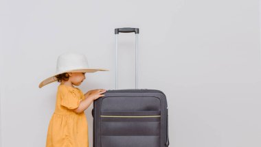 Büyük bir bavulun yanında beyaz şapkalı küçük bir kız. Çocuklar bir tatil konsepti istiyor. Beyaz arkaplan kopyalama alanı